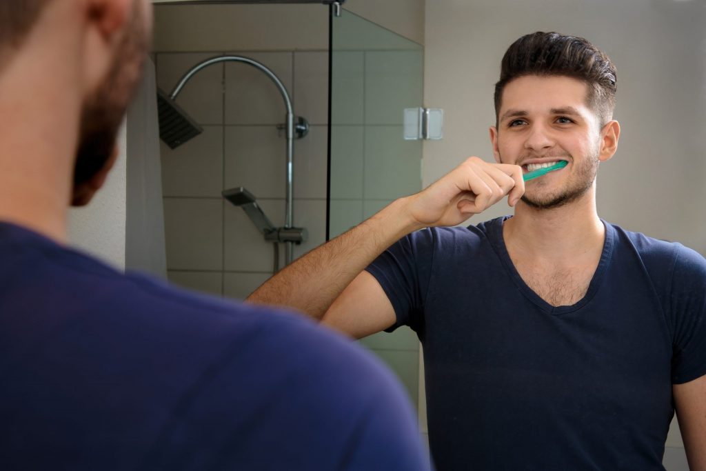  Man brushes his teeth in front of his bathroom mirror, using a whitening toothpaste.