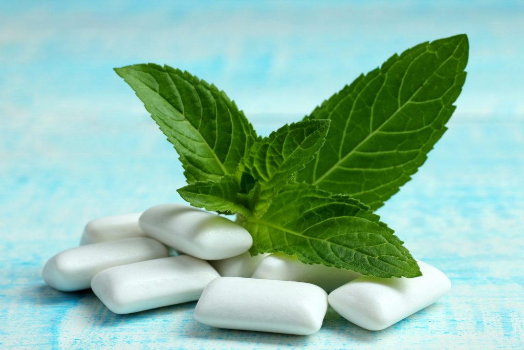  A small pile of white gum tablets with green mint leaves resting on top to suggest the flavor.