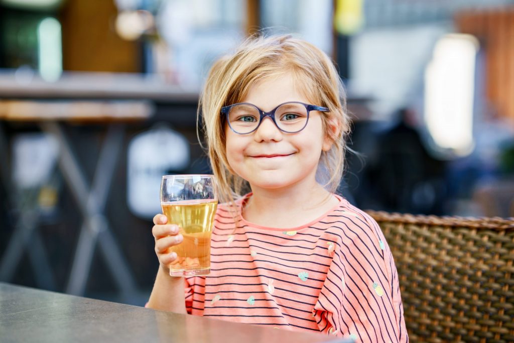 Elementary school-age girl smiles and holds glass of apple juice, which isn’t one of the best drinks for teeth.  