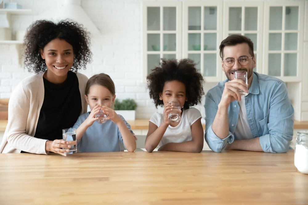  Mother, daughters, and father sit at a kitchen table drinking water, having chosen drinks that are good for your teeth. 
