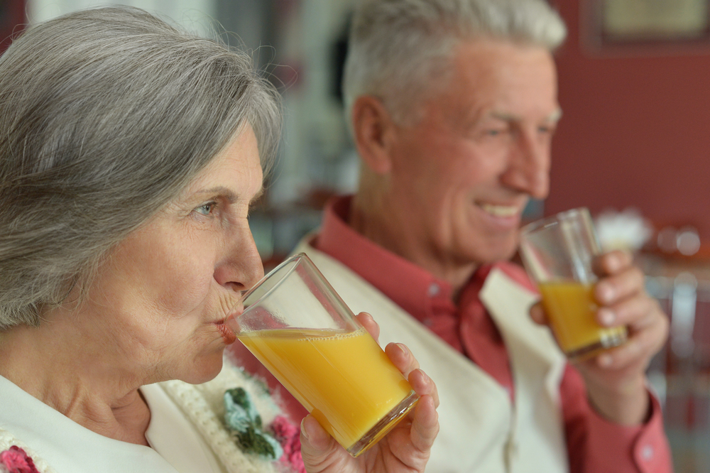  Woman and man in kitchen smile as they drink orange juice, which is high in citric acids and isn’t the best drink for your teeth.