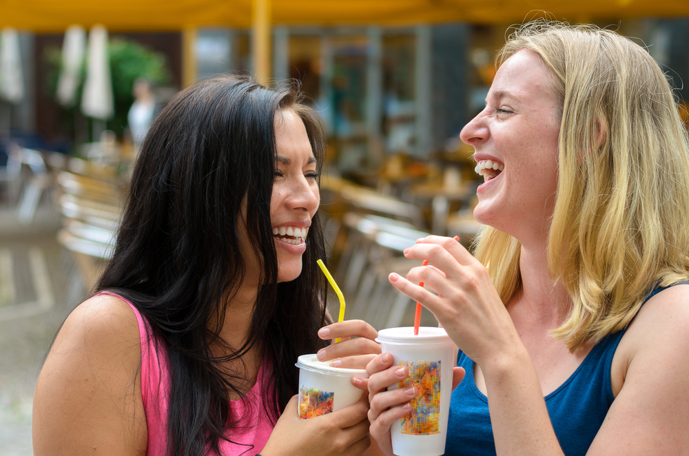  Two teenagers smile and laugh as they drink sugary drinks through a straw, limiting their teeth’s exposure to the sugars.