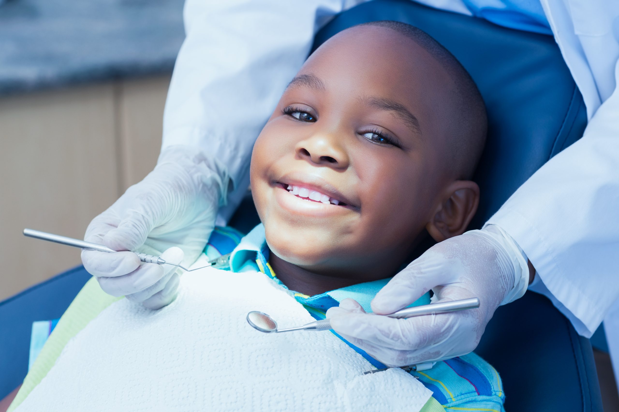 A smiling boy in a dental chair with a dentist holding examination instruments.