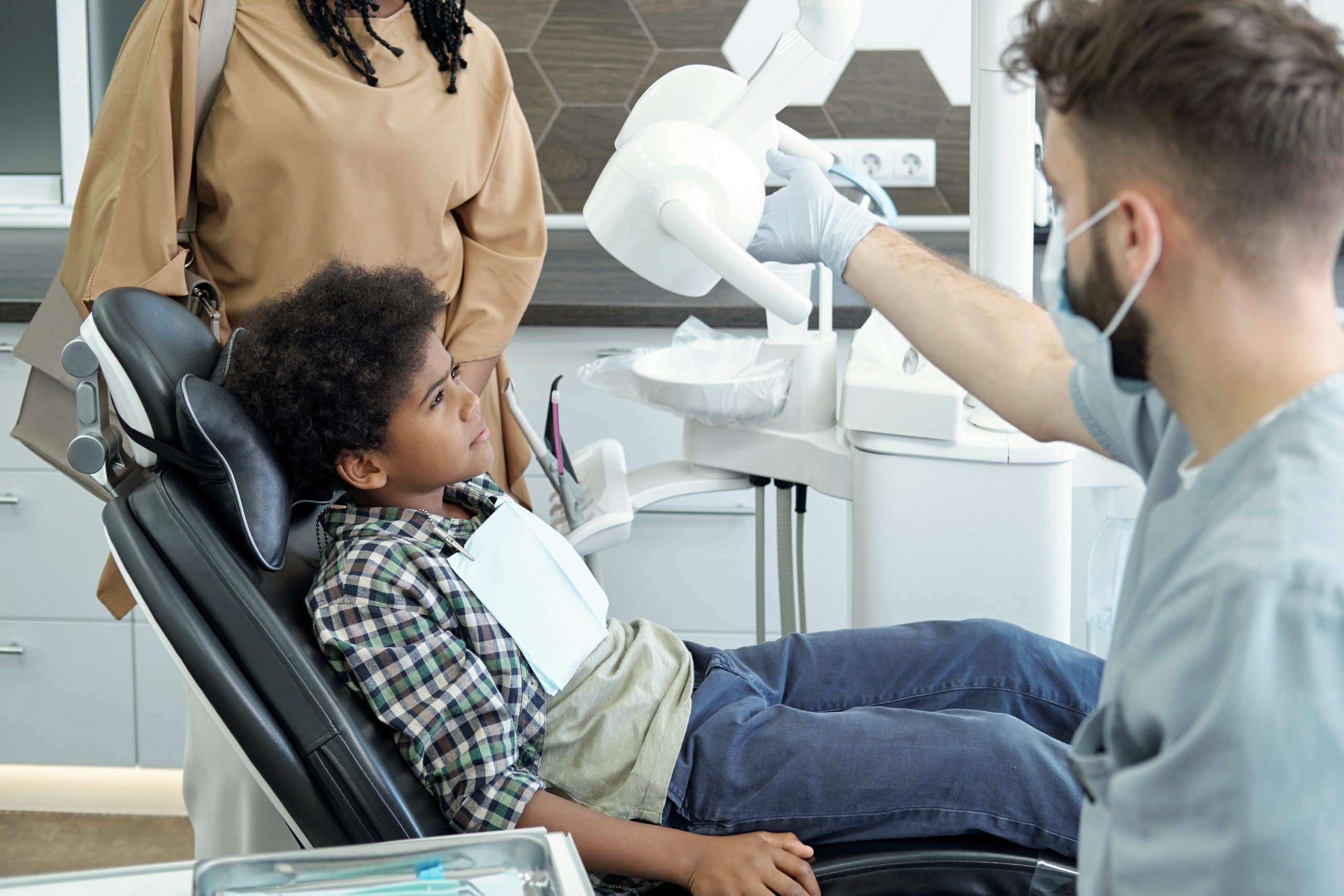 A young boy being examined at the dentist with his mother overlooking. 