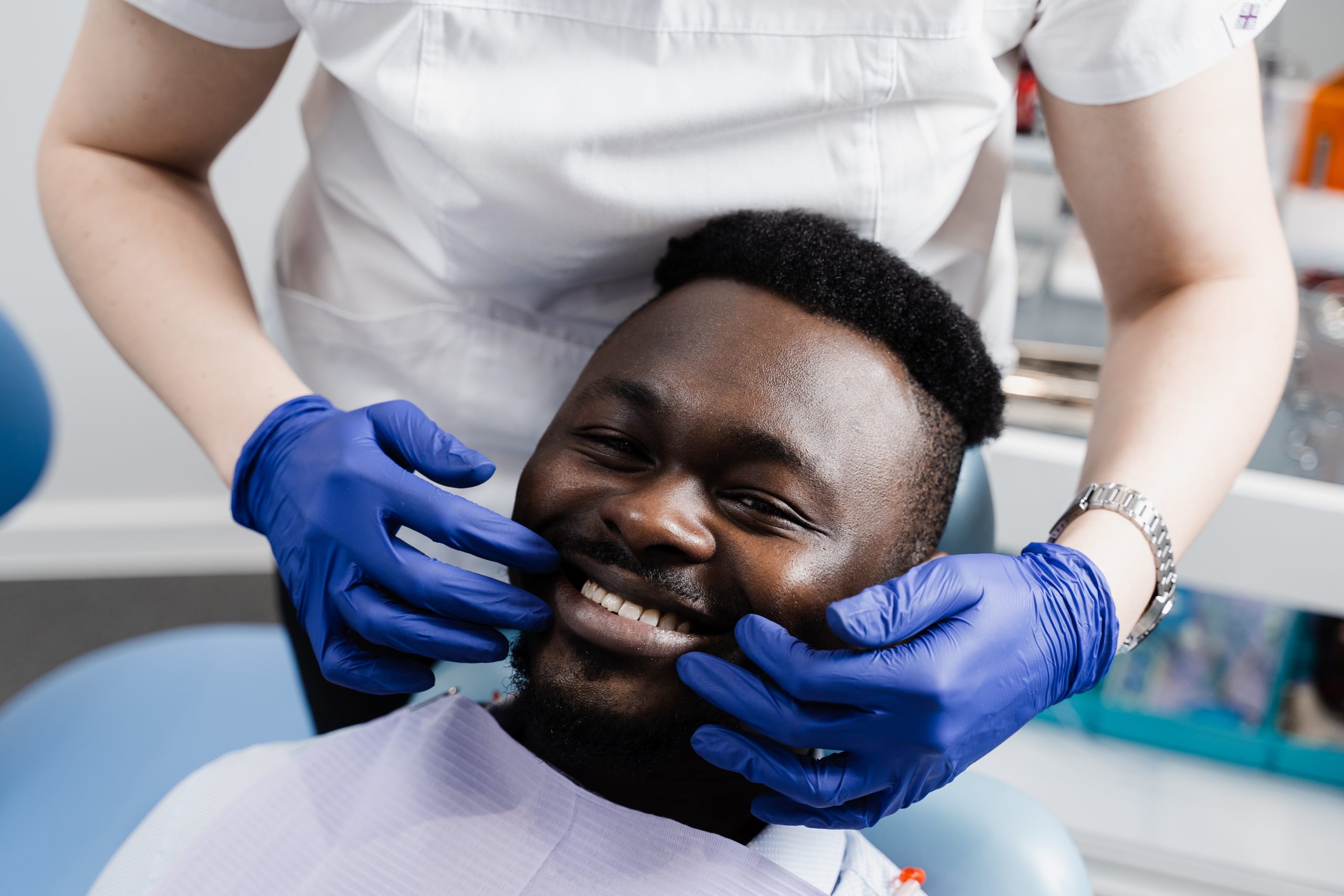 A man reclines in a dental chair and smiles as a gloved dentist examines his teeth and screens for oral and oropharyngeal cancer.