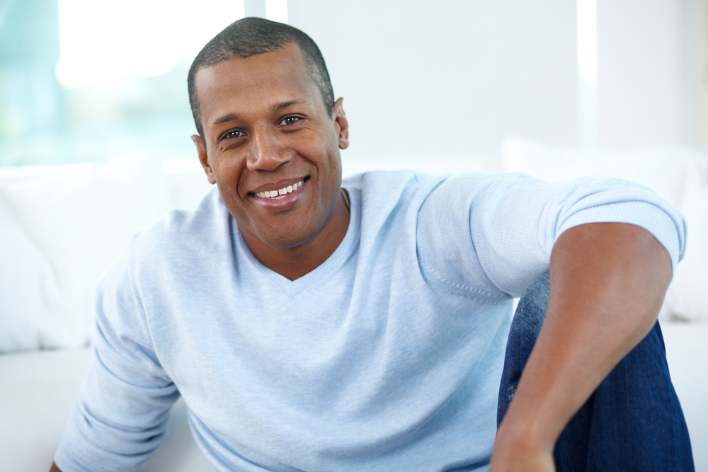 A man smiles while sitting casually on his couch after his oral surgery procedure has occurred. 