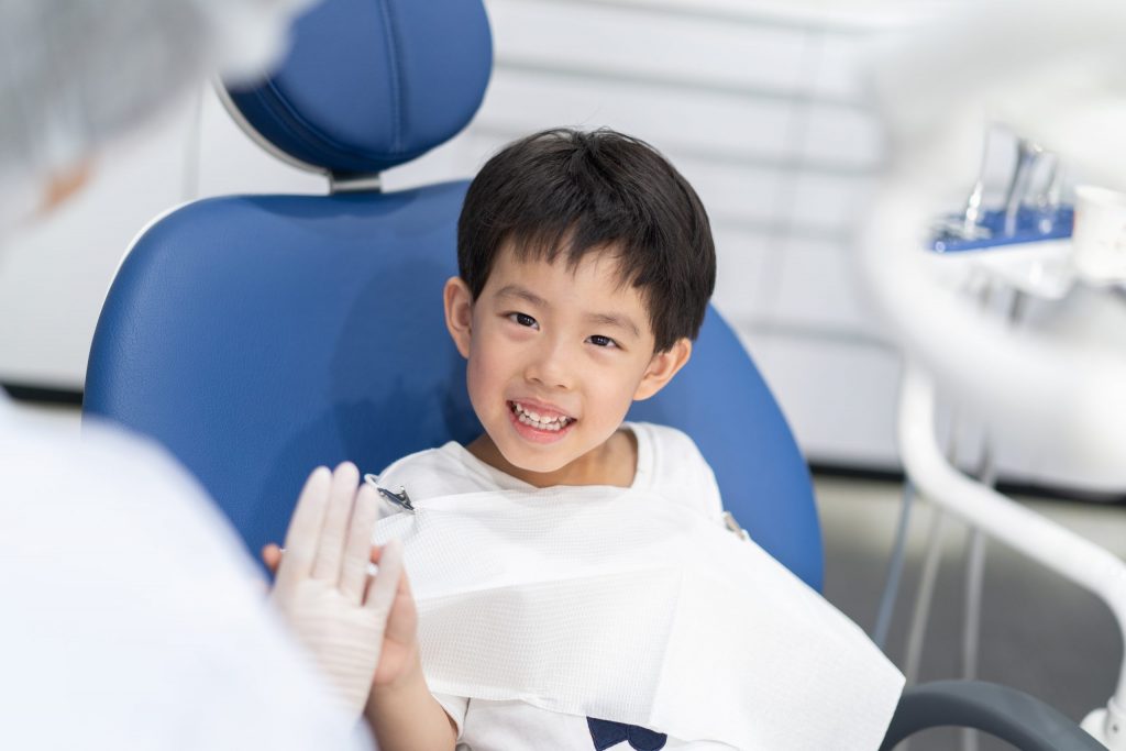 A young boy in a dental chair gives his dentist a “high five” and smiles, feeling no pediatric dentist anxiety.