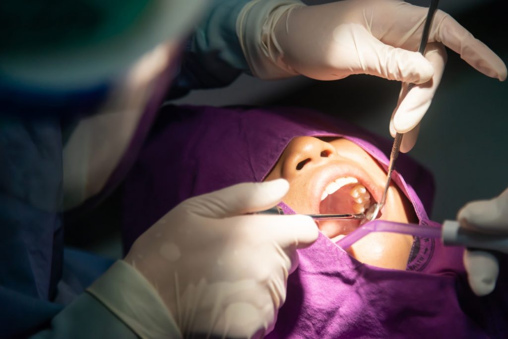 A dentist performs wisdom tooth extraction surgery on a young person.