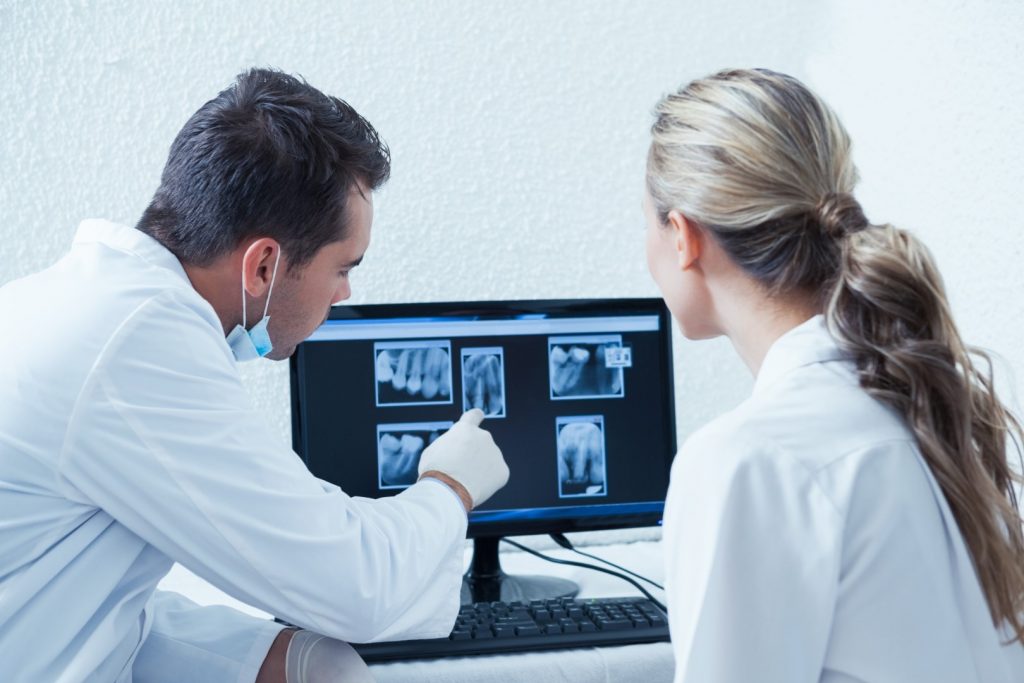 Two oral cancer doctors look at X-rays on a monitor.