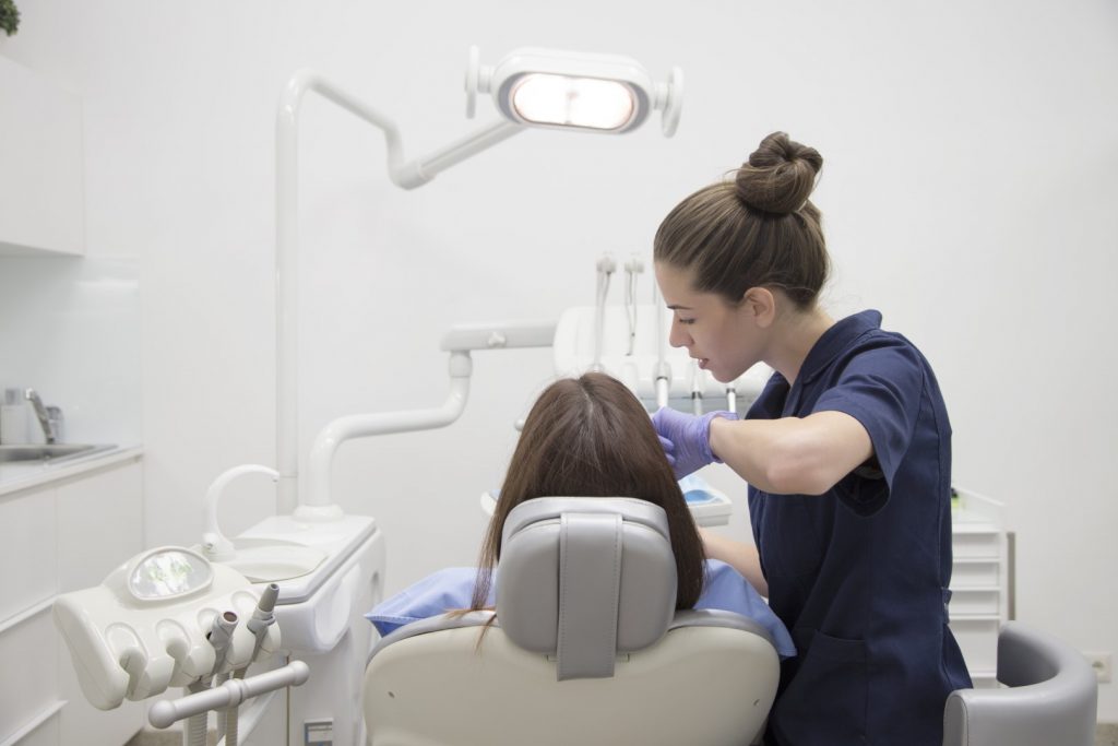  A dentist is filling tooth decay for a woman reclining in a dental chair in a dentist’s office.