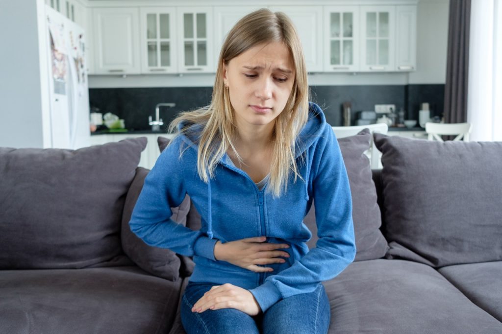 Woman holds her hand to stomach, feeling nauseated after having swallowed some oil while oil pulling for teeth.