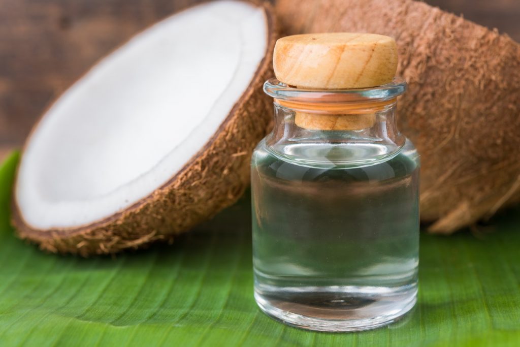 Coconut cut in half sits on table with stoppered glass bottle of coconut oil, illustrating coconut oil pulling for teeth.