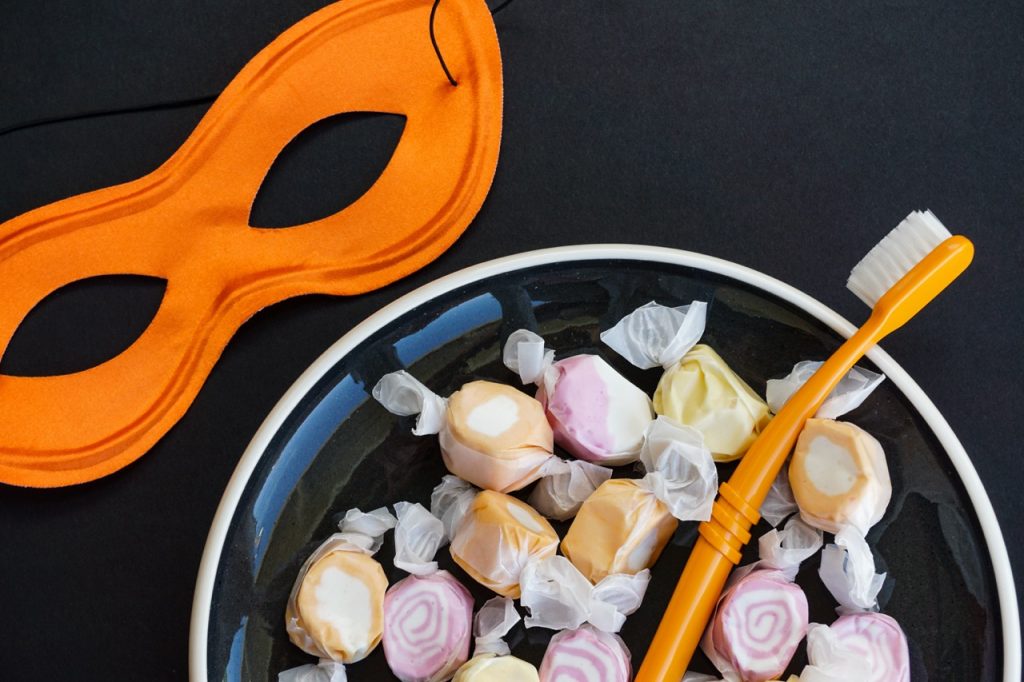 An orange mask is placed next to a bowl of candy with an orange toothbrush in it.