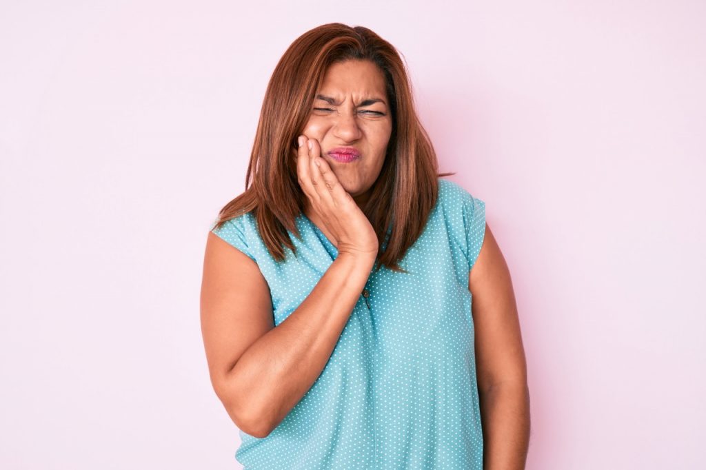 A young woman holds her hand to her jaw as she wonders if there is a connection between Halloween candy and teeth pain.