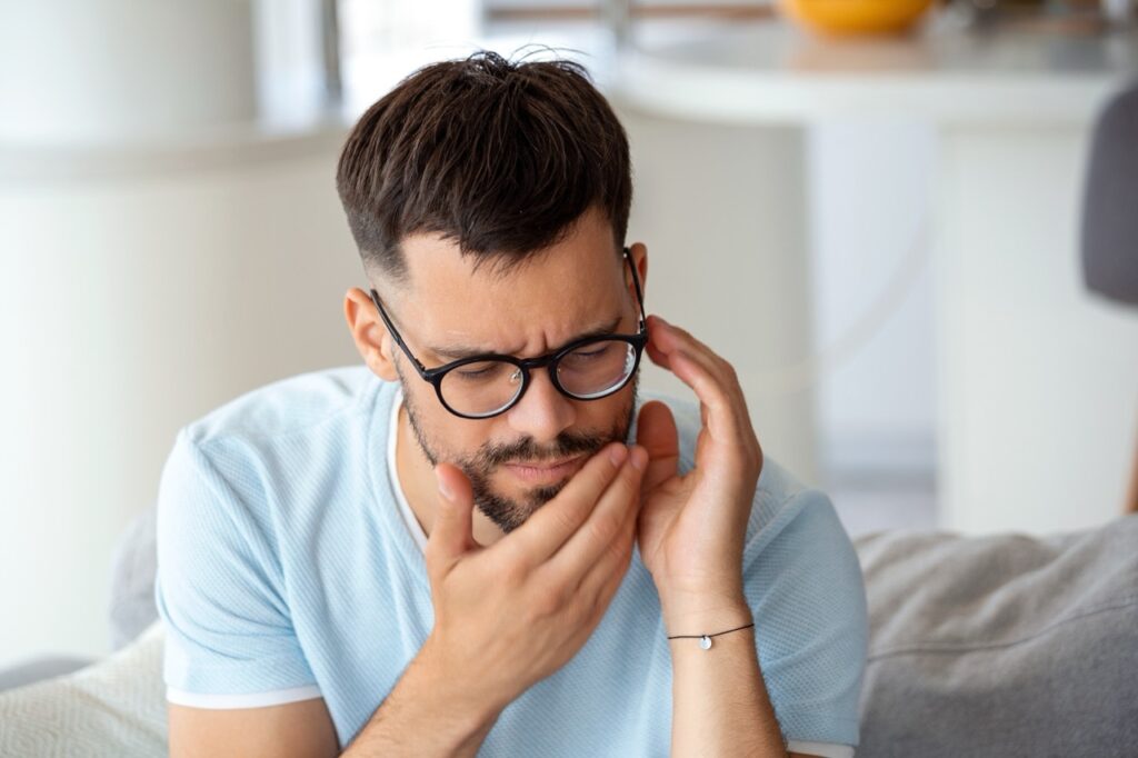 Man holds hands to his chin, indicating he feels pain and may need wisdom teeth removal. 