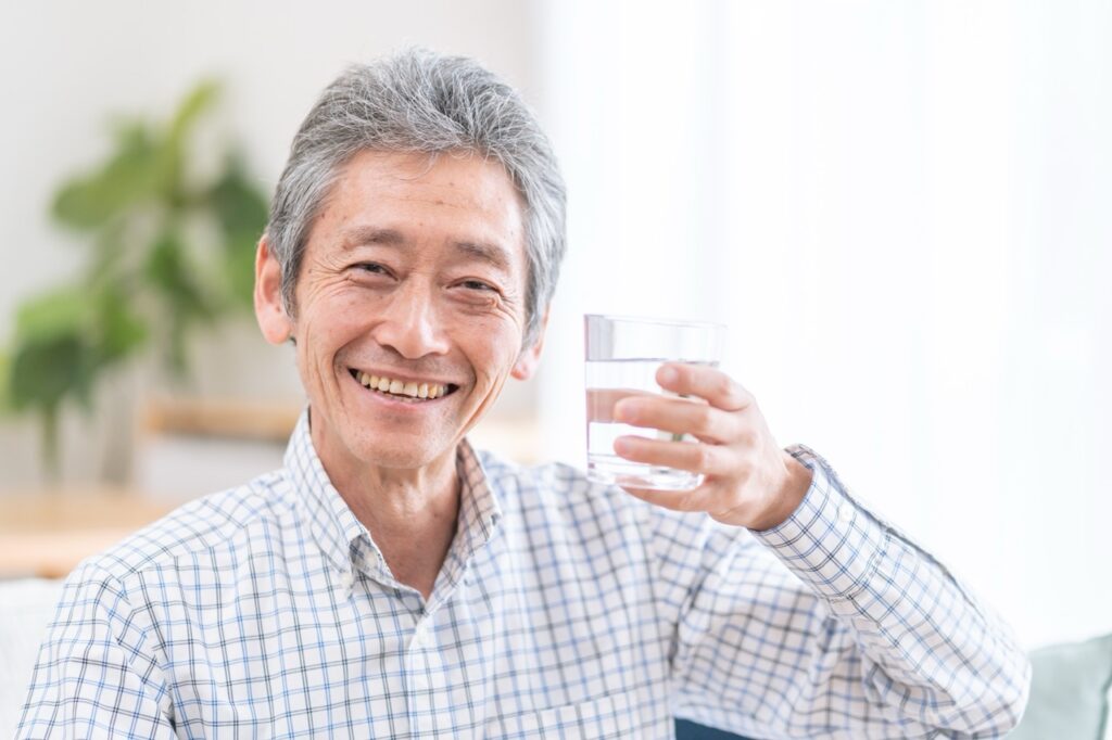 Senior man smiles as he holds a glass of fluoridated water. 