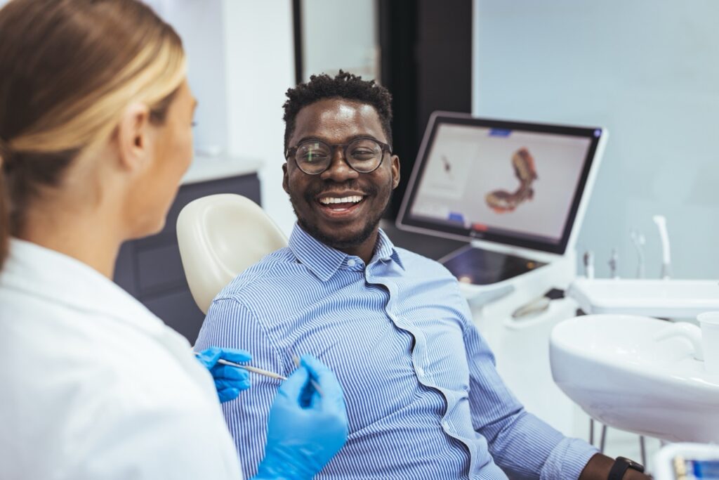 Patient sits in dental chair, smiling at his oral surgeon after procedure, happy his orofacial pain and headache have been relieved.