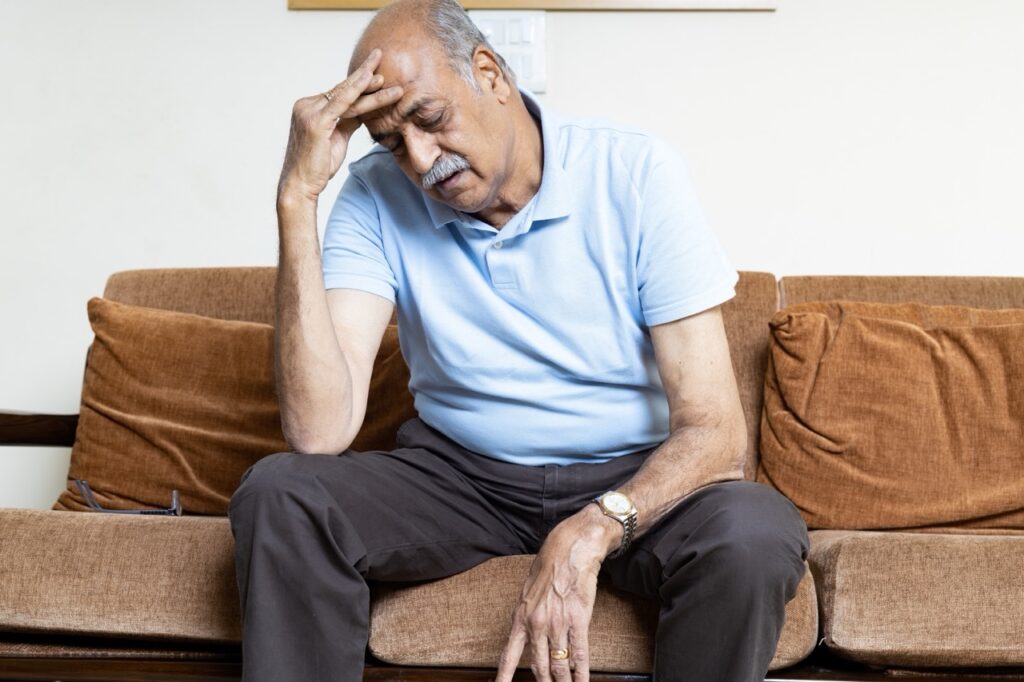 Man sits on couch rubbing his forehead, suffering from orofacial pain and headache. 