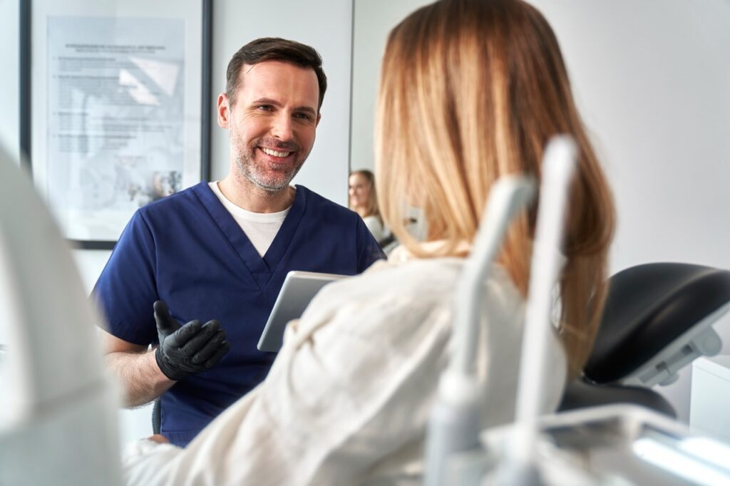 Dentist consults with breast cancer patient who reclines in dental chair before examination.