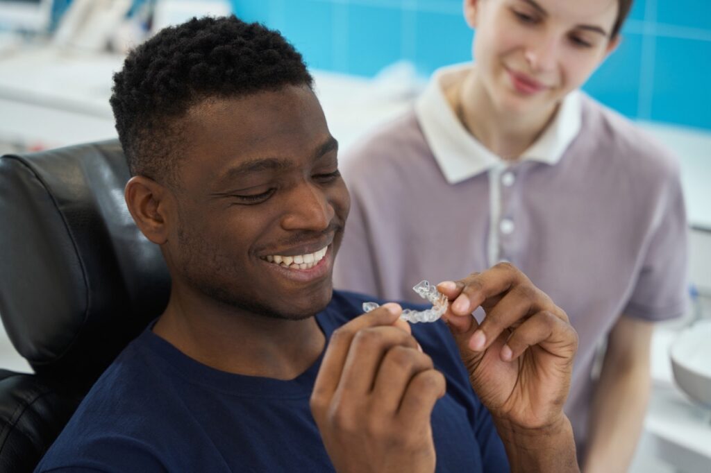 Dentist watches smiling man seated in dental chair try on his invisible aligners, designed and made with digital dentistry.