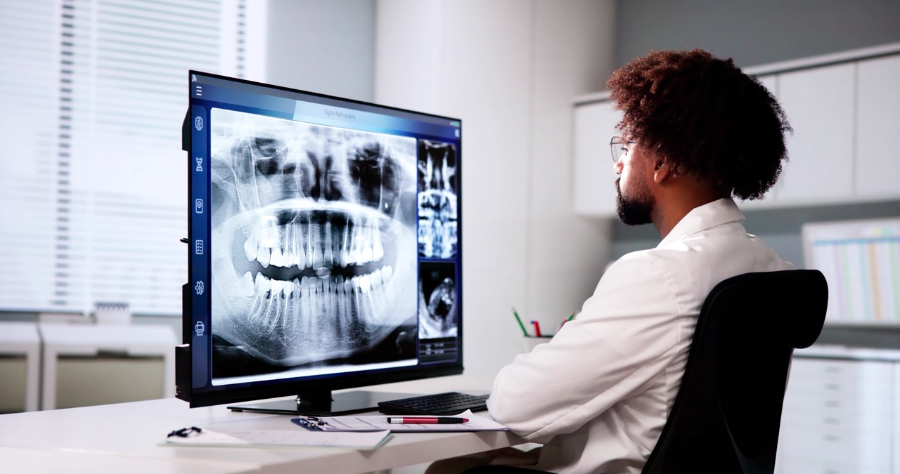 Dentist reviews AI-enhanced digital imaging of his patient’s mouth on a computer monitor.