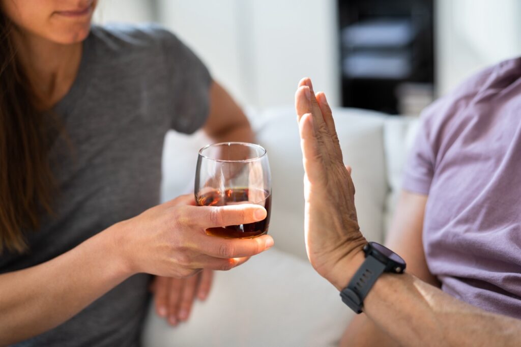 Man refuses glass of brandy offered to him by woman, concerned about the effects of alcohol on teeth. 