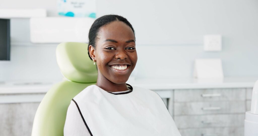 Woman sitting in dental chair, wearing apron for digital radiography in dentistry, smiles a big, bright smile.