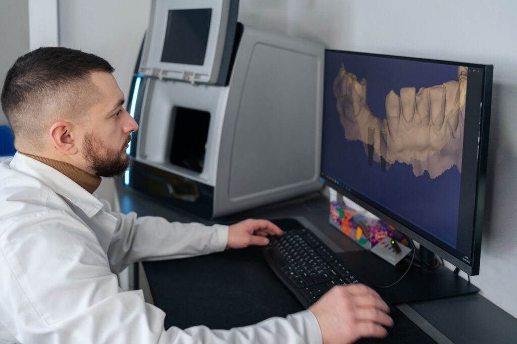 Dental lab technician reviews digital model of lower teeth on a computer monitor, preparing to print dental appliance.