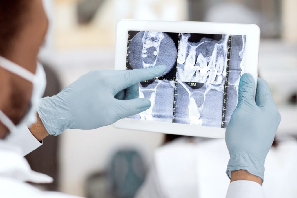 Masked and gloved dentist examines X-rays of patient’s teeth produced using artificial intelligence in dental radiology.