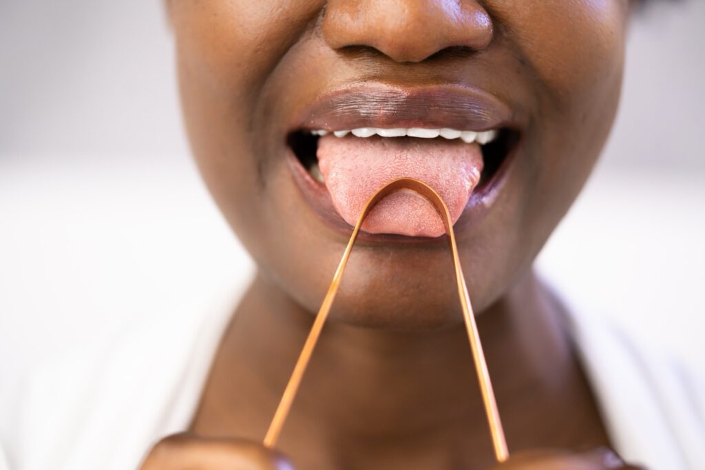 Woman uses tongue scraper to clean the surface of her tongue. 