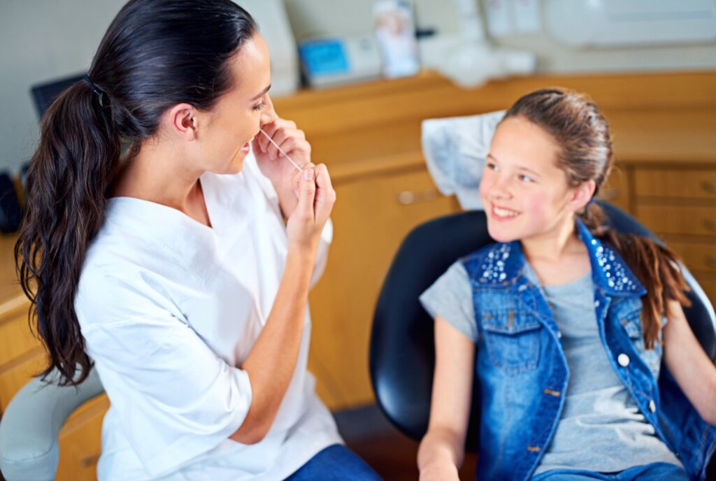 Dentist discusses importance of flossing with and demonstrates proper flossing technique to tween girl patient in dental chair.