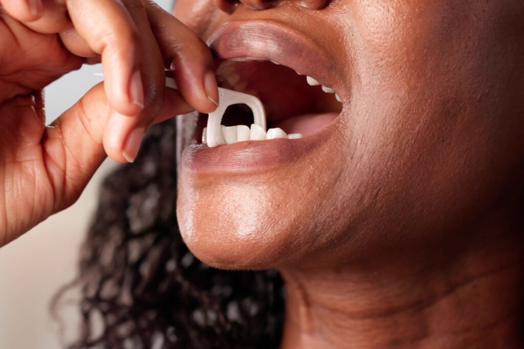 Woman uses plastic floss holder to help her floss between her lower teeth.