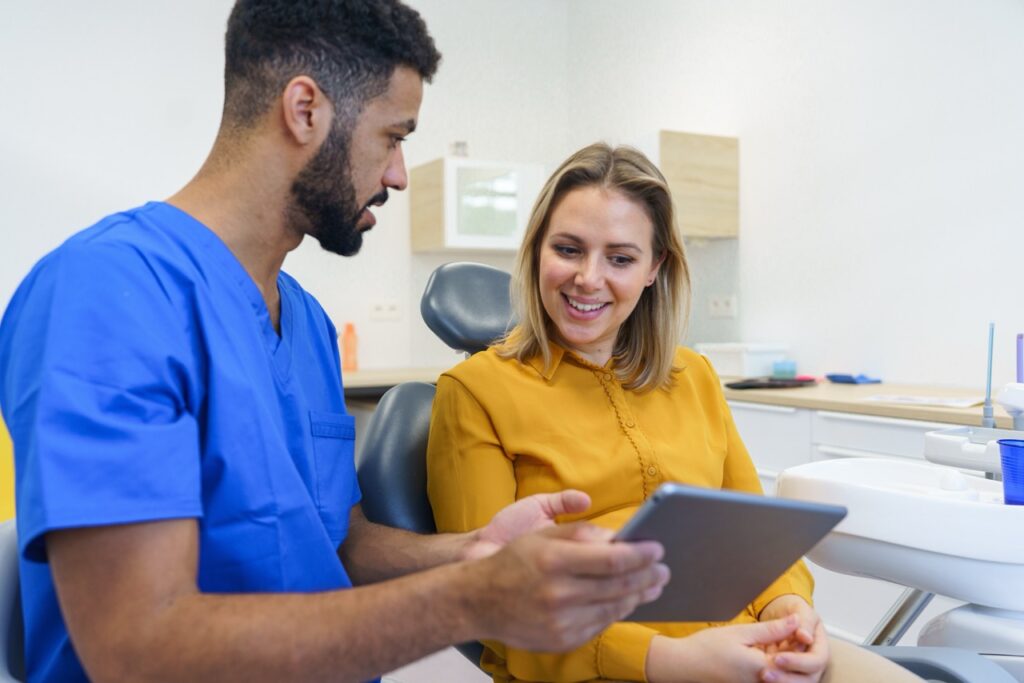 Dentist holding tablet computer consults with woman sitting in dental chair about ways to keep her oral microbiome healthy. 