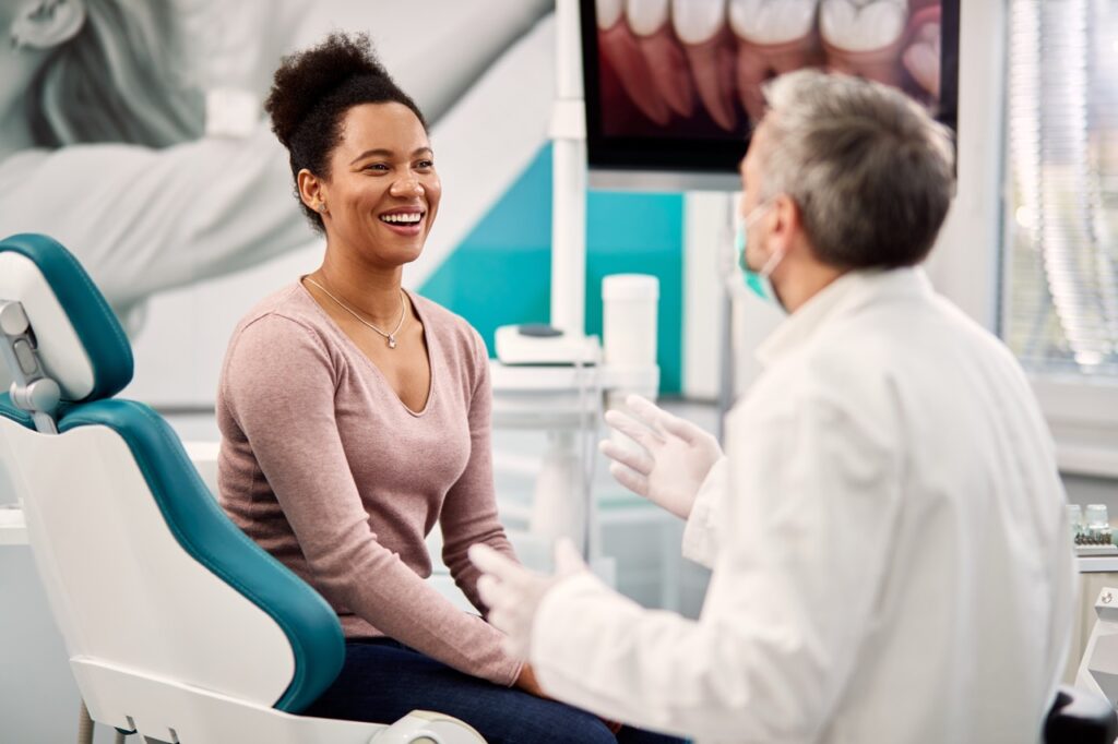Woman sitting on dental chair smiles as she talks with her dentist about the benefits of fluoride in water.