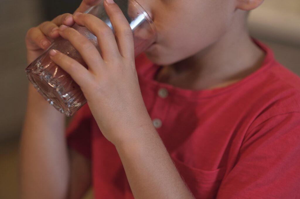 Young elementary school-age boy drinks glass of fluoridated water.