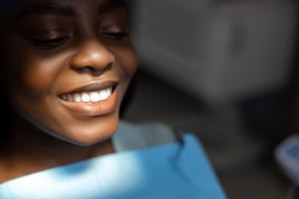 Woman smiles as she sits in dental chair after receiving dental cleaning. 