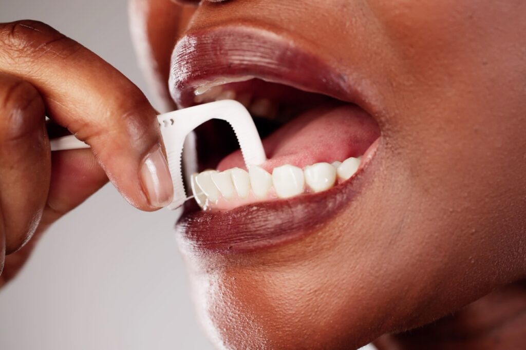 Woman is using floss pick for flossing teeth. 