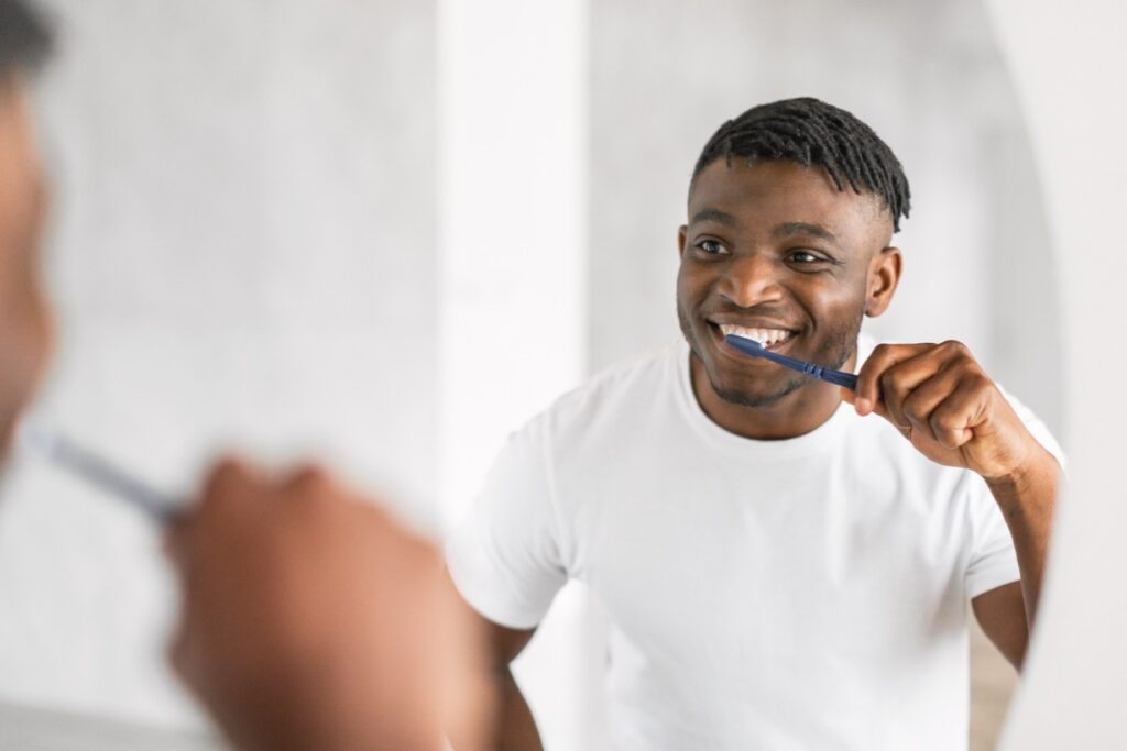 Man looks at himself in mirror as he brushes his teeth. 