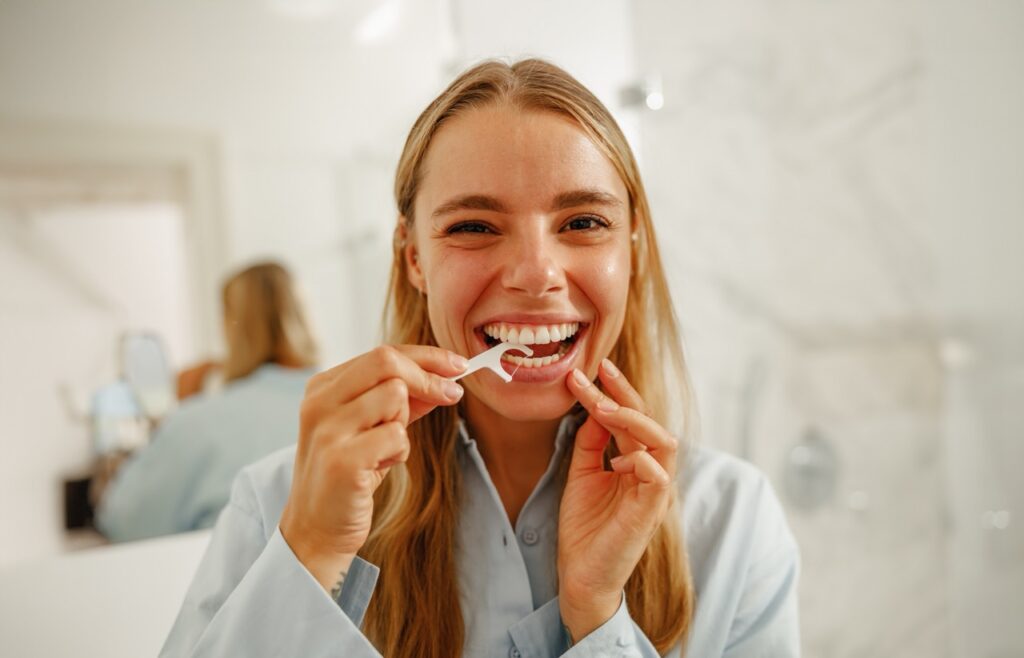 Woman uses interdental pick for flossing her bottom teeth. 