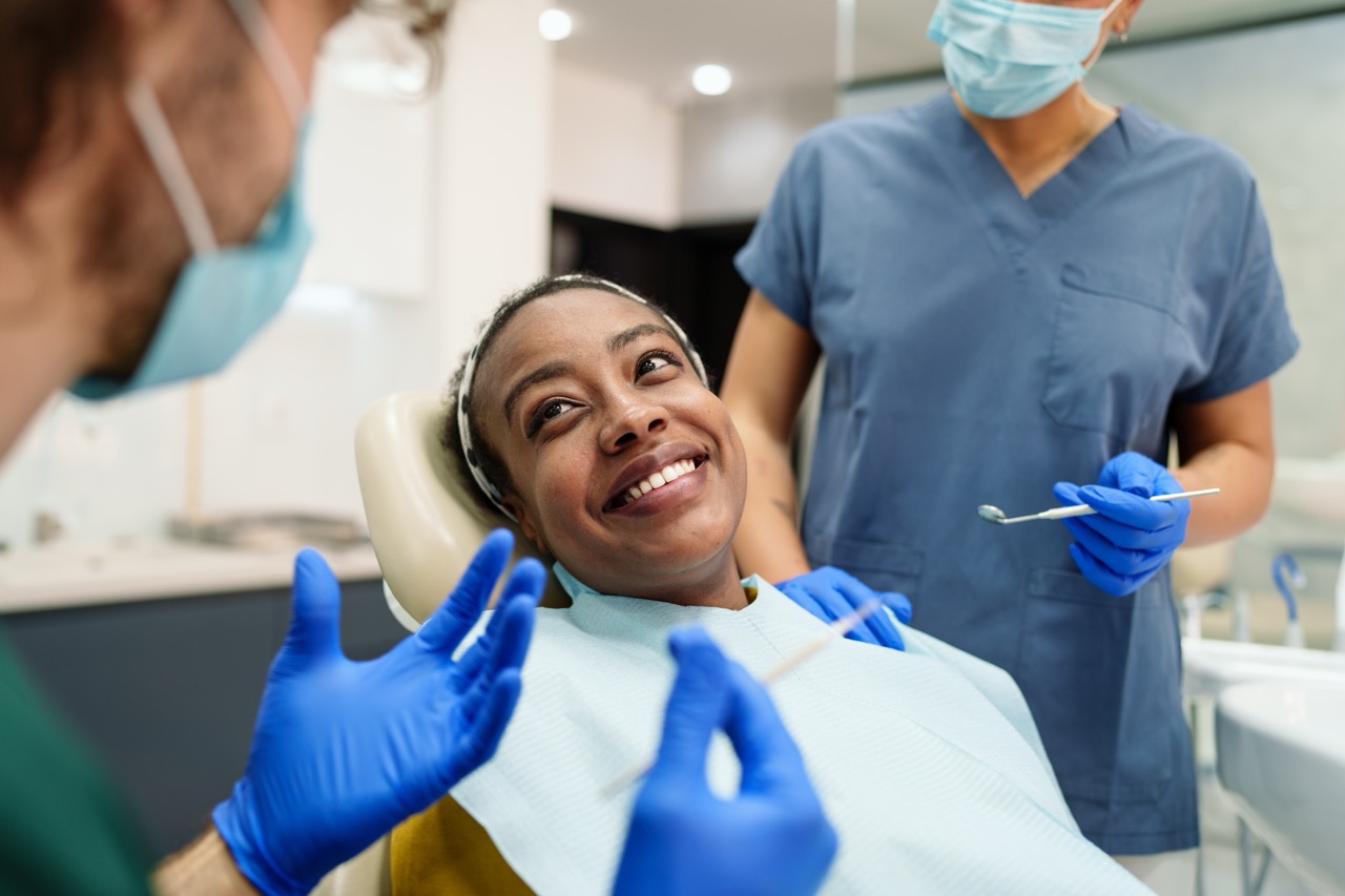 Woman reclining in dental chair smiles as dentist and dental hygienist prepare to examine and clean her teeth.