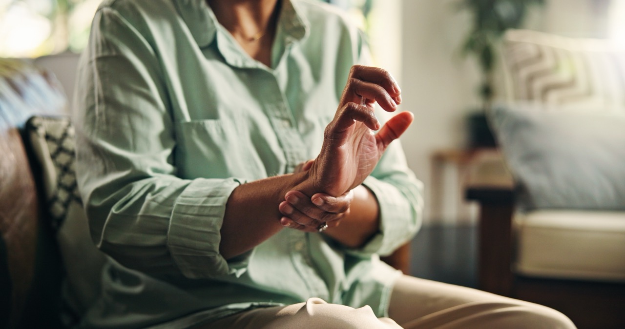 Senior woman sits in chair, rubbing her right wrist to ease the pain of her arthritis. 
