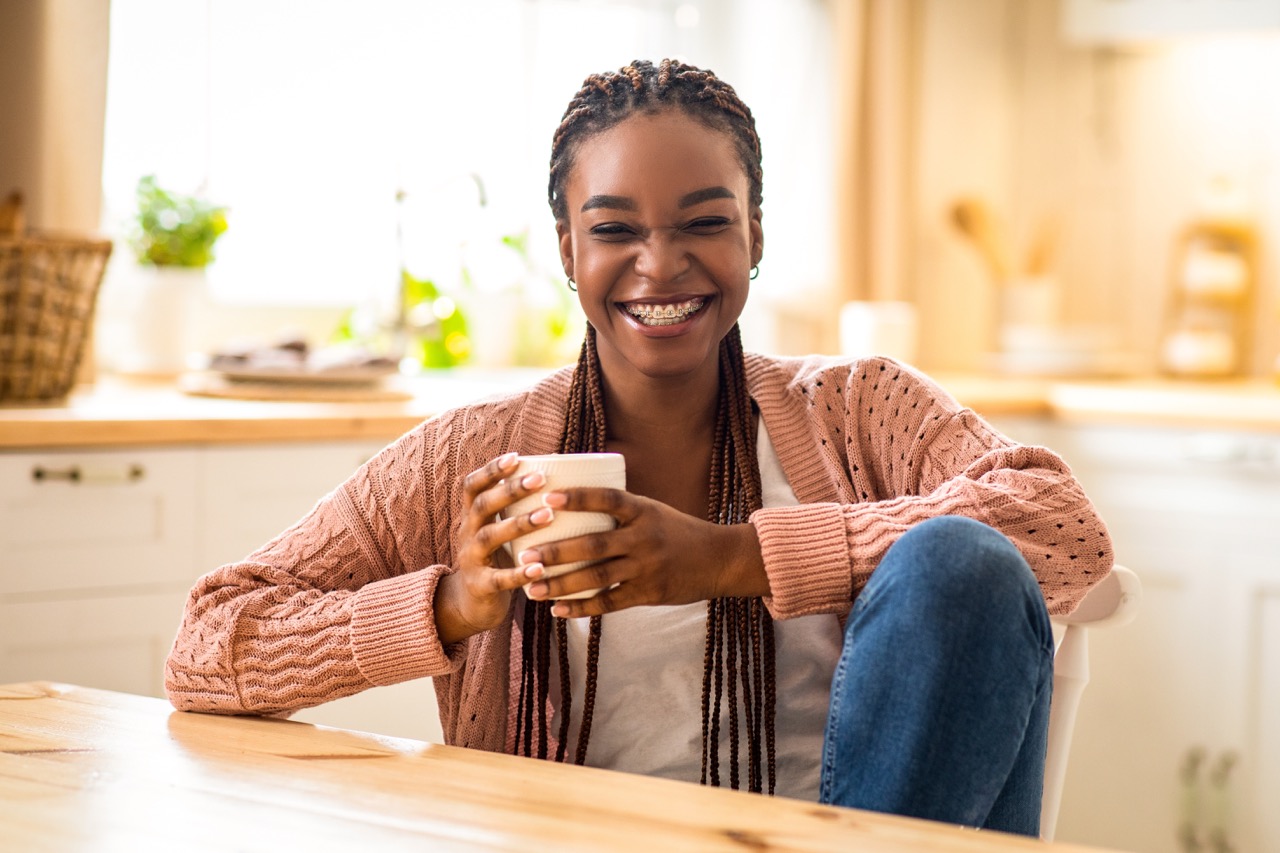A young woman holds a coffee mug and smiles because she no longer 
