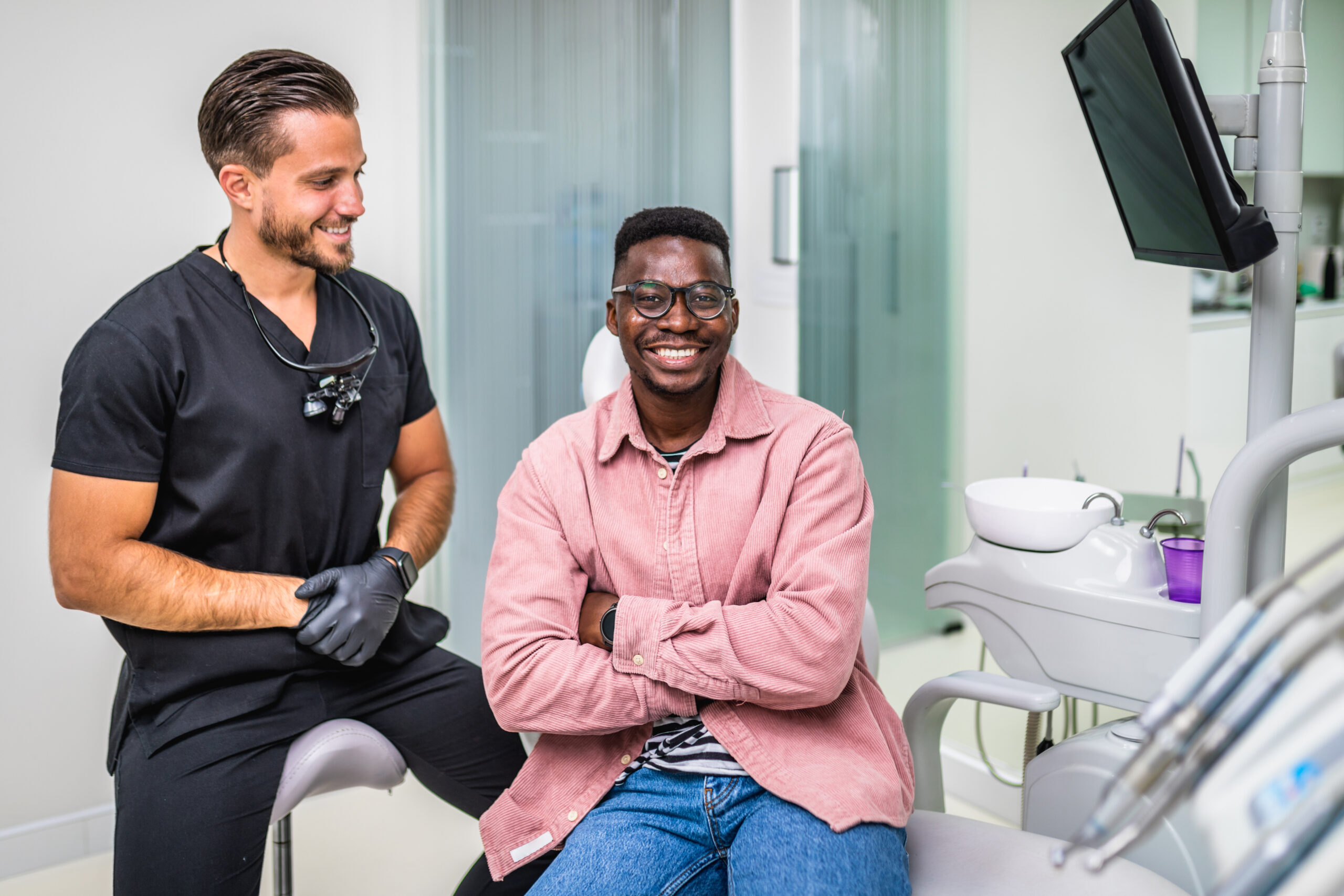 Dental patient sits in dental chair after digital dentistry treatment, smiling big, bright smile, as his dentist looks on.