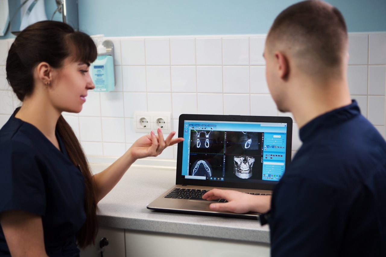Two dentists analyze X-rays of a patent’s jaw using AI-enhanced image analysis.