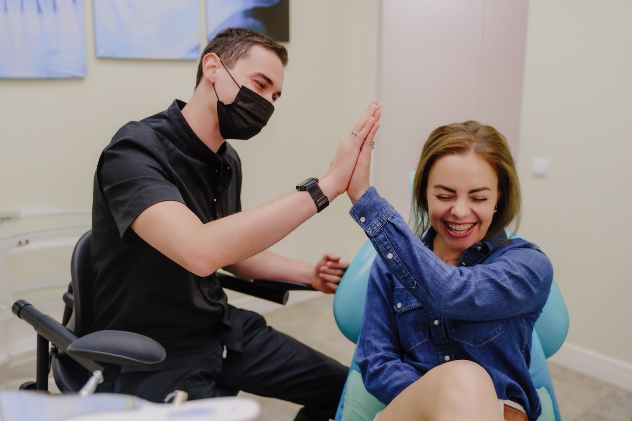 Woman sitting in dental chair laughs and gives her dentist a high five after a successful root canal procedure.