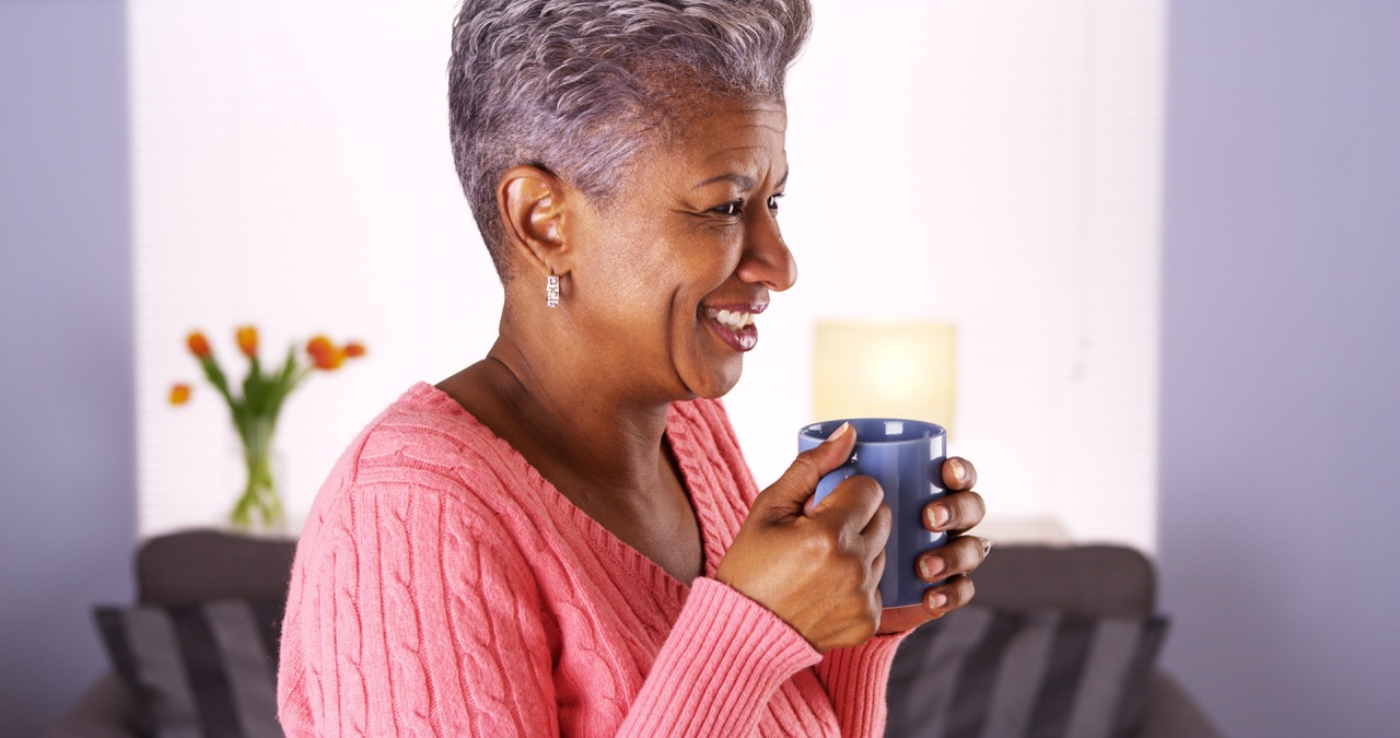 Woman smiles big, bright, beautiful smile as she holds her morning mug of coffee.