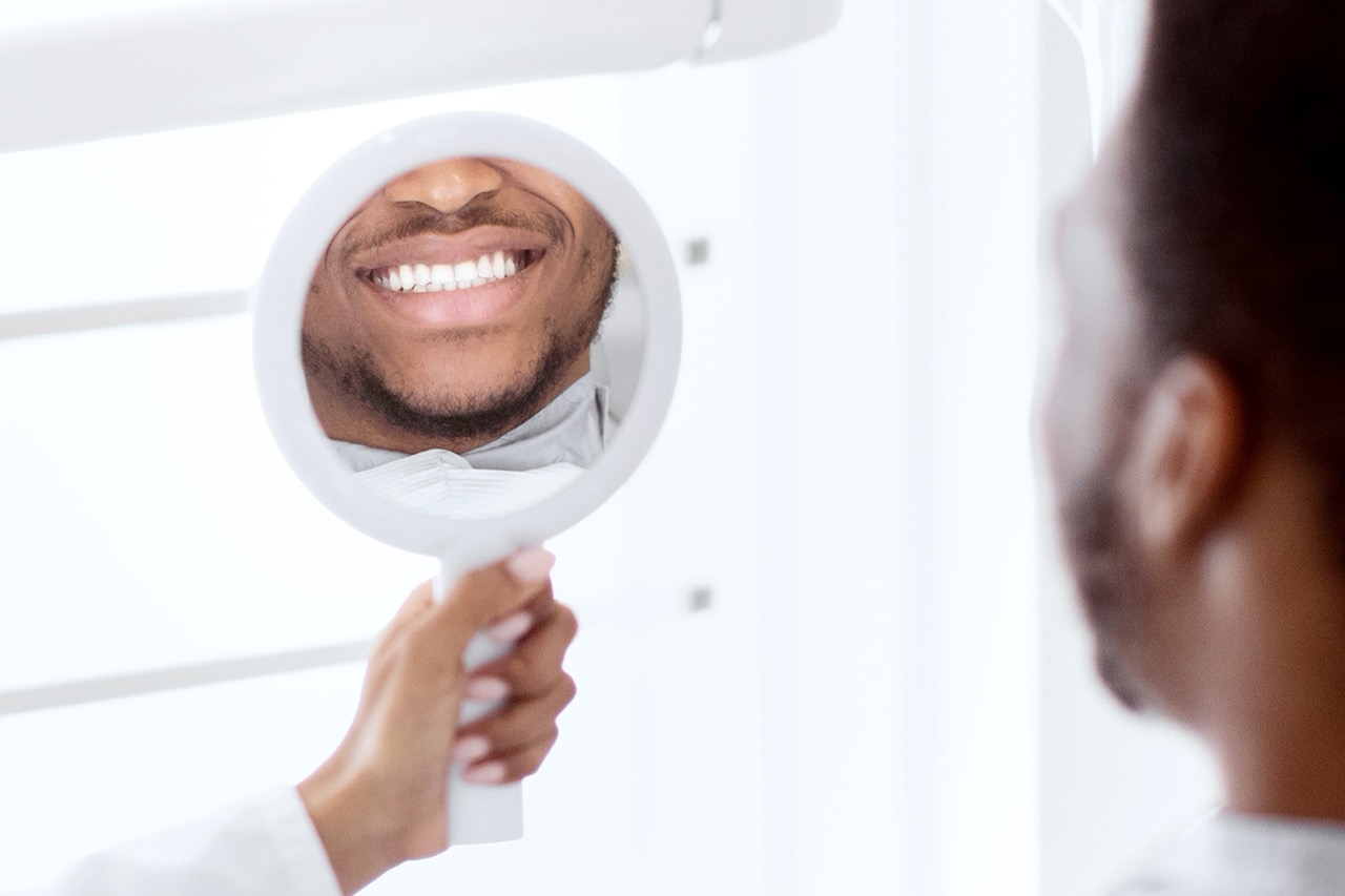 Man sitting in dental chair looks at his smile in handheld mirror, enjoying results of laser dentistry treatment. 