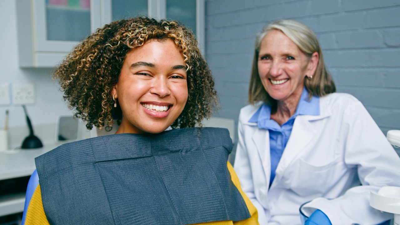Patient sitting in dental chair and her dentist smiles after successful laser dentistry treatment. 