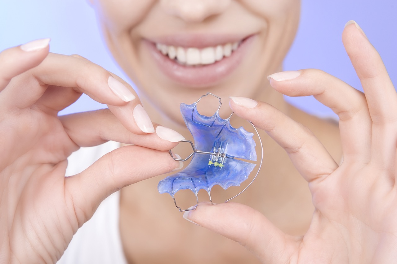 Smiling woman holds a blue, traditional Hawley retainer